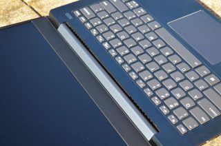 Výdech ventilátoru v žlábku mezi základnou a krytkou pantů obrazovky.